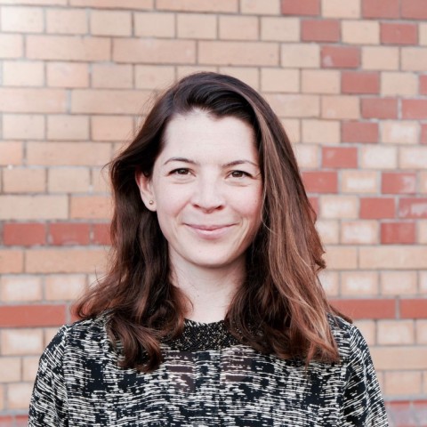 Tabea Leukhardt with long brown hair in front of a brock wall smiling