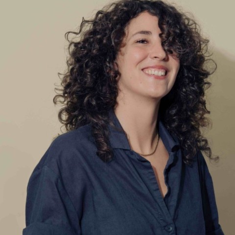 Milena Mana da Costa mit gelocktem schwarzem Haar lacht in die Kamera