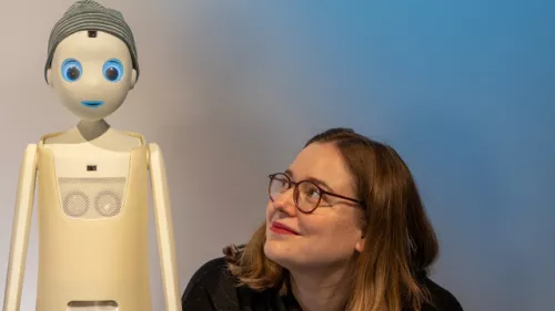 Katharina neben einem humanoiden Roboter mit Mütze.
