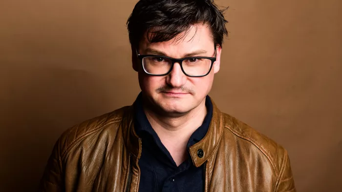 Sebastian Gießmann in Lederjacke vor einem braunen Hintergrund