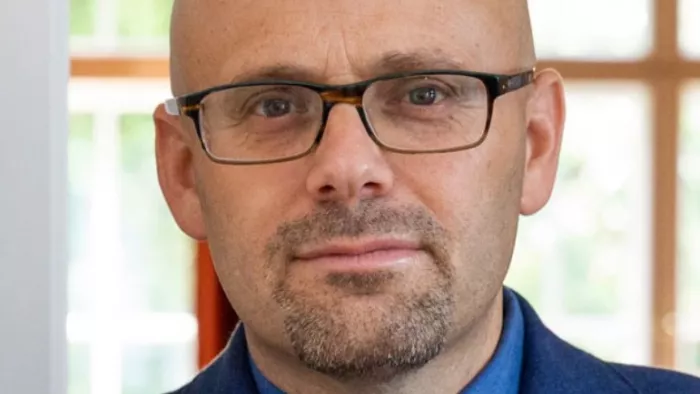 Daniel steht vor einem Fenster. Er trägt eine Brille.