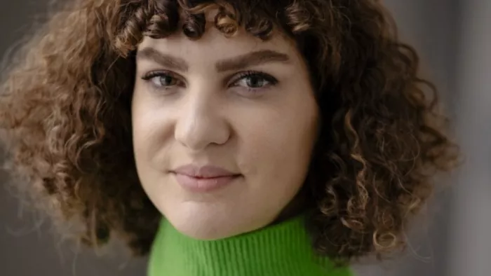 Portraitfoto von Laura Wiesböck. Sie trägt schulterlange, lockige Haare, einen Pony sowie einen Rollkragenpullover. Laura lächelt in die Kamera.