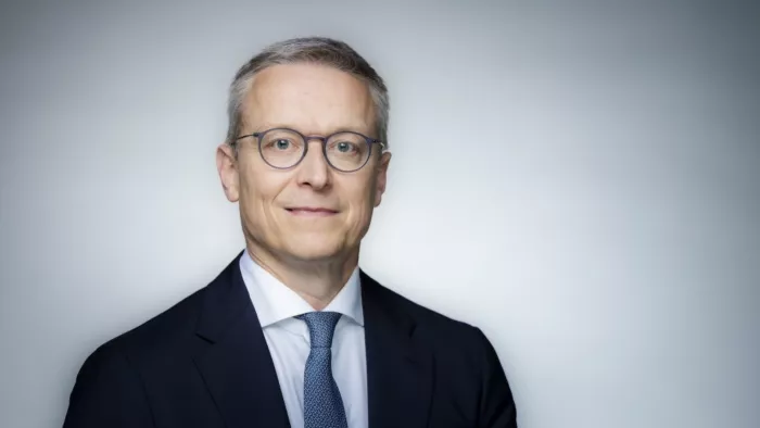 Foto von Karsten Wildberger. Er trägt kurze Haare, Brille, Anzug und Krawatte. Dabei schaut er in die Kamera.