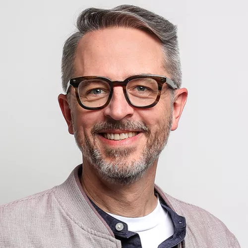 Tapio Liller, Mann mit grau meliertem Bart, lächelnd, mit einer markanten Hornbrille