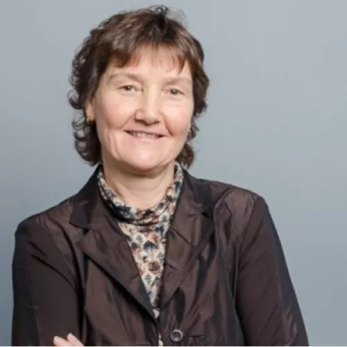 Regina Gnirss trägt einen Blazer und lächelt in die Kamera. Sie hat kurze Haare.