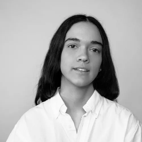 Black-and-white headshot of a person with long dark hair wearing a white button-up shirt against a plain background.