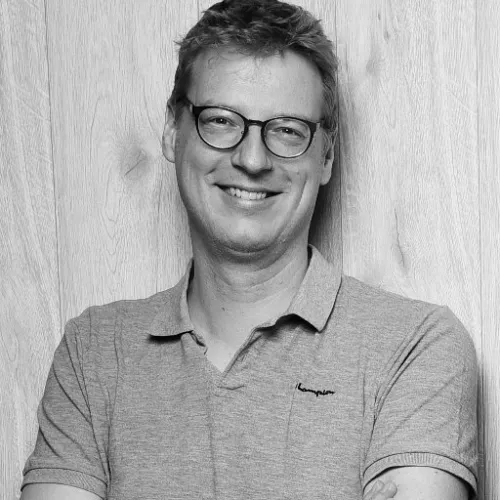 Schwarz-Weiß Foto von einem Mann mit Brille, der in die Kamera lächelt.