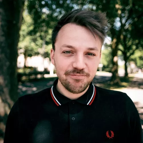 Ein Foto von Gavin Karlmeier. Einem Mann, der im schwarzen Poloshirt in einem Park steht. Sein Bild ist in die Kamera gerichtet.