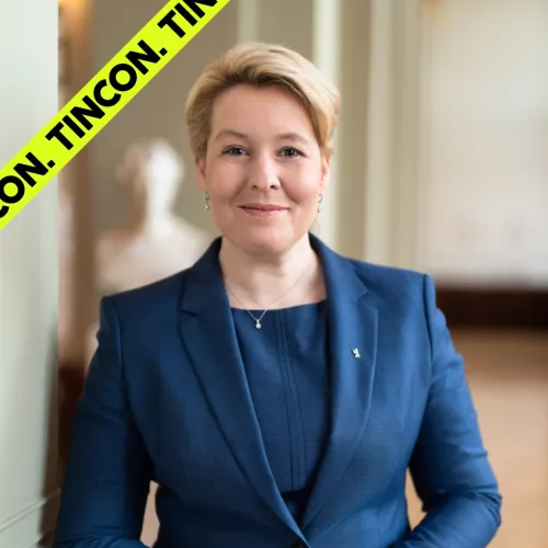 Eine Frau lächelnde mit blonden Haaren, zu einer Frisur zusammengesteckt, in einem blauen Anzug lächelt