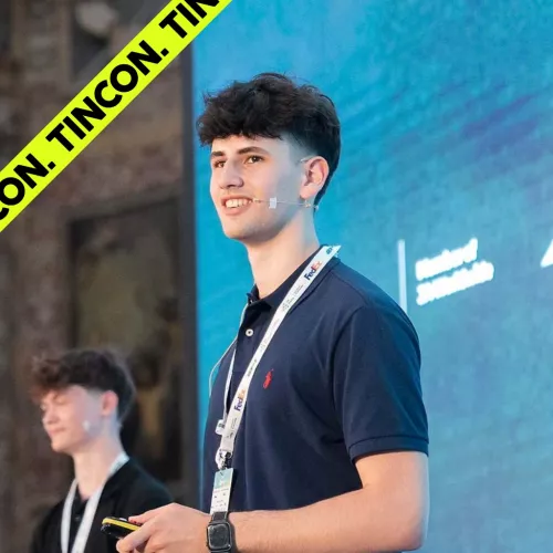 Junger Mann mit kurzem, lockigem Haar und einem Lanyard um den Hals, hält einen Vortrag
