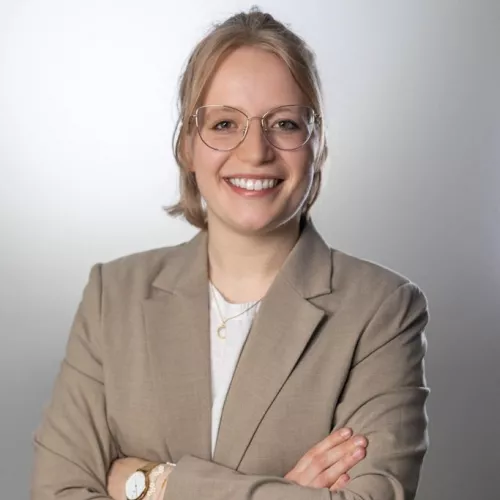 Bild einer weiblich gelesenen Person mit beigem Blazer, Brille und blonden Haaren