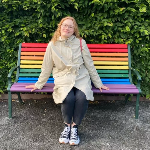 Inga Gostmann sitzt auf einer bunten Bank, die wie ein Regenbogen angestrichen ist.