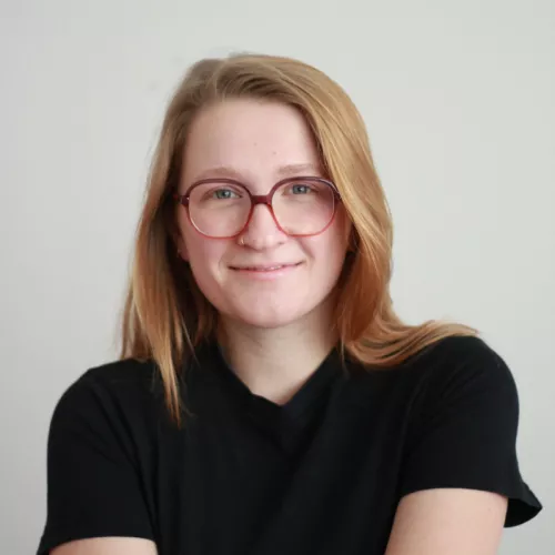 Foto von einer weißen weiblich gelesenen blonden Person mit Brille in einem schwarzen T-Shirt.