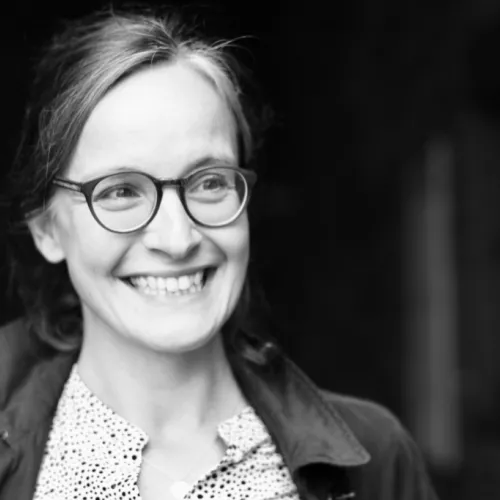 Schwarz-Weiß-Aufnahme von Anne Gräfe, am linken Bildrand stehen, lächelnd nach rechts aus dem Bild raus blickend