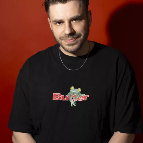 Das Biild zeigt Jean-Philippe Kindler im schwarzen T-Shirt vor rotem Hintergrund - lächelnd. 