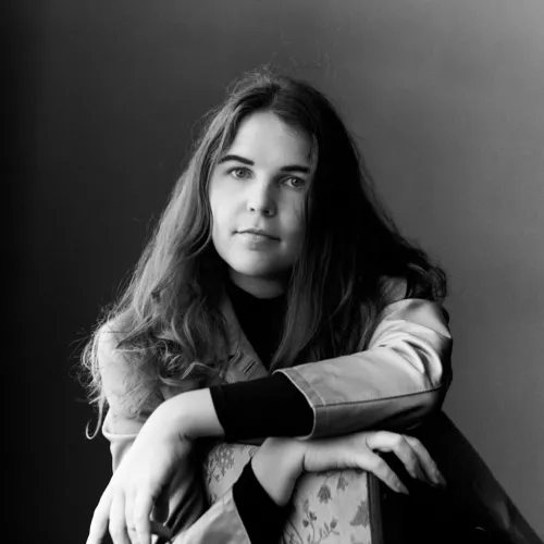 woman with long brown hair pictured sitting on a chair, in black & white