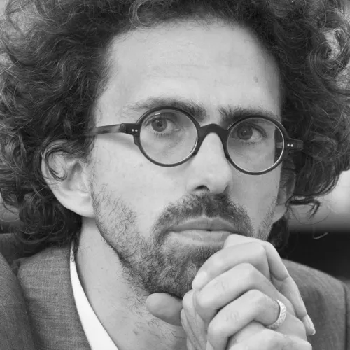 Niccolo Milanese with curly hair and round glasses and a short beard