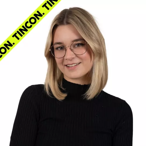 Junge Frau mit schulterlangen, blonden Haaren und Brille, trägt einen schwarzen Rollkragenpullover und lächelt