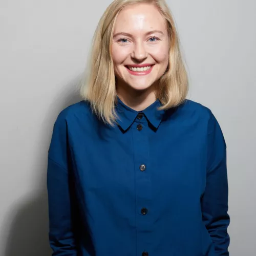 Foto von Julia Christina Hess vor grauem Hintergrund mit blauer Bluse.