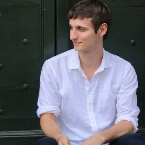 Person mit weißem Hemd sitzt vor grüner Tür.