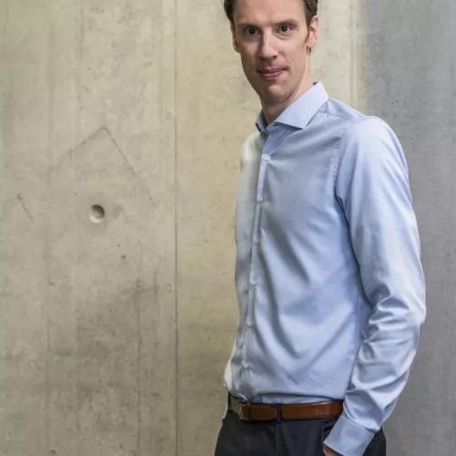 Björn Ommer im blauen Hemd vor grauer Betonwand