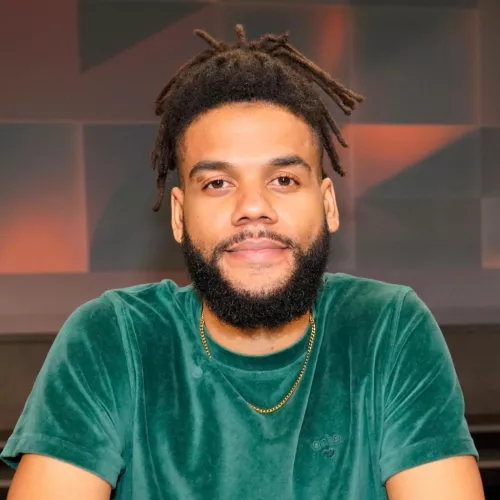 Philipp Awounou ist vor einem geometrischen Hintergrund in Rot- und Grautönen zu sehen, er trägt ein grünes T-Shirt.