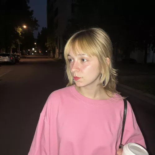 dzennifer is standing on a street with a pink t-shirt. 