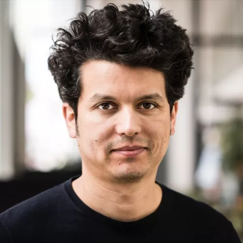 Profilbild von Semir Chouaibi.  Er trägt dunkles, lockiges Haa, zeigt einen neutralem Gesichtsausdruck, und blickt direkt in die Kamera. Semir trägt ein dunkles Oberteil; der Hintergrund ist unscharf und wirkt wie ein heller Innenraum.